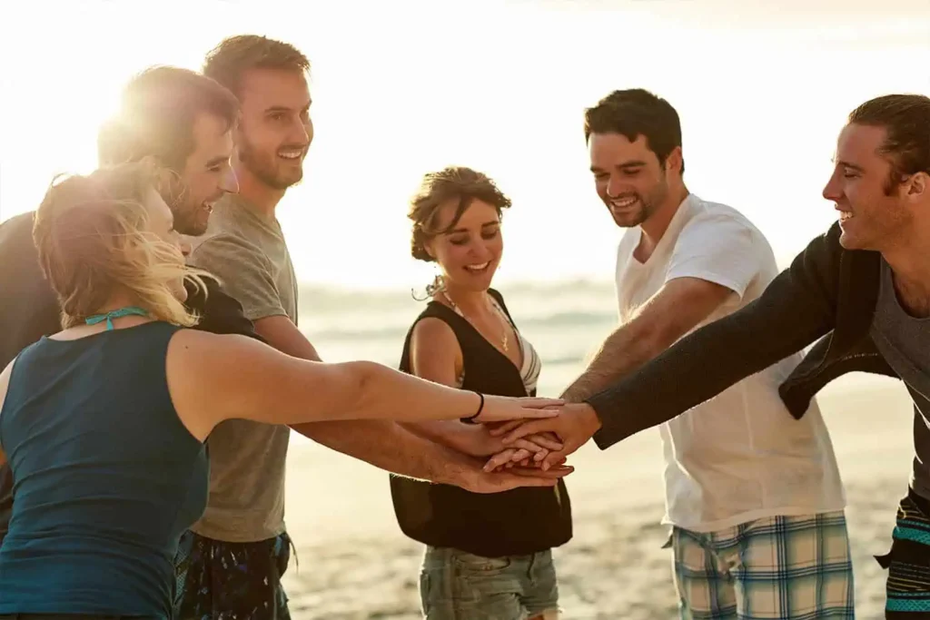 Group of friends joyfully joining hands on the beach during sunset.